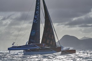 The trimaran Réauté Chocolat with the island of Guadeloupe in the background as he races to the finish line