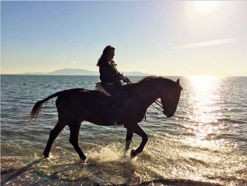 Un'amazzone su un cavallo Maremmano nella baia di Talamone al tramonto
